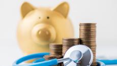 A piggy bank next to a pile of coins and a stethoscope 